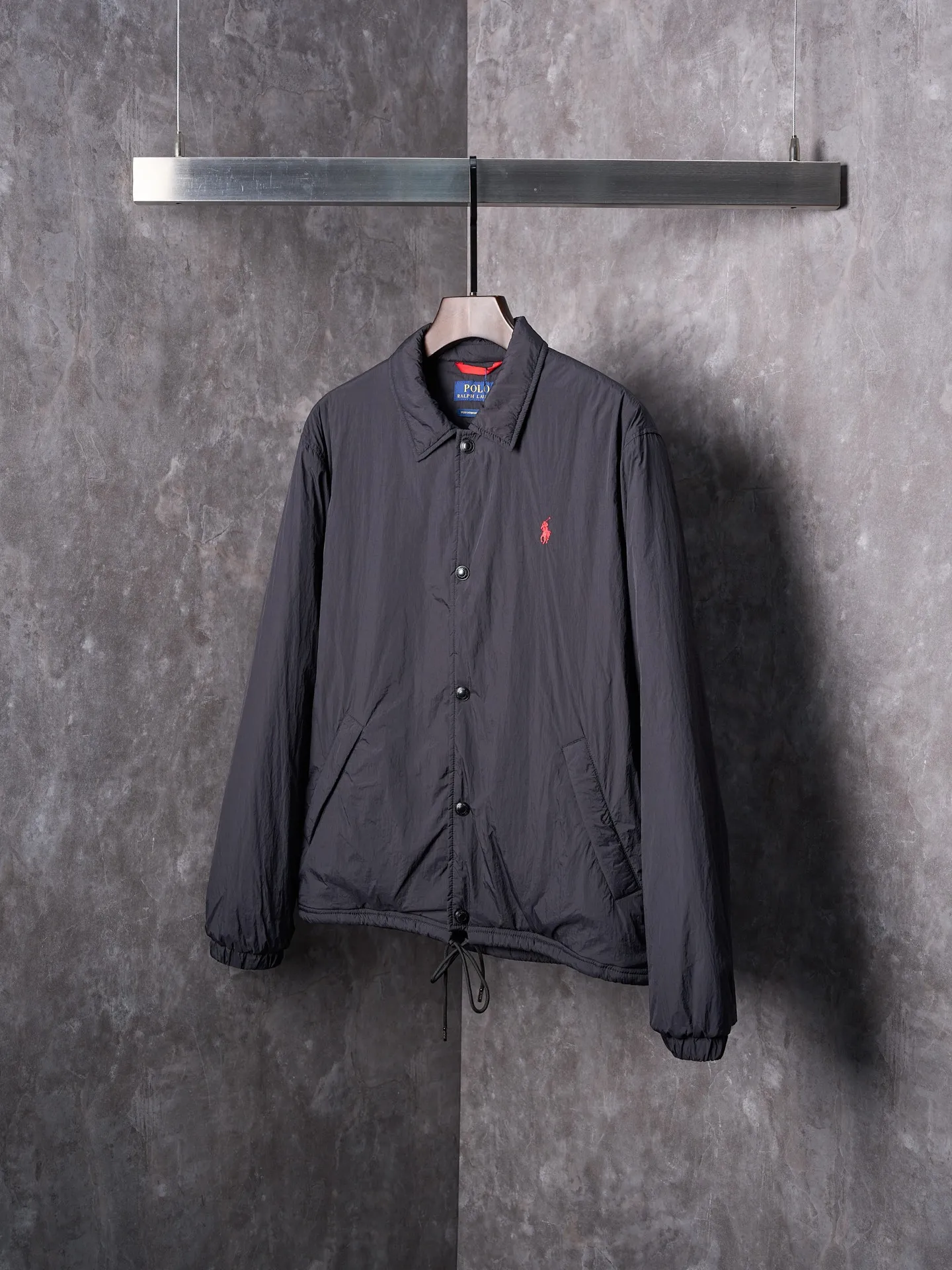 P640 Actual auction] Ralph Lauren/Ralph Lauren Pony Red Label lightweight cotton lapel coach jacket [Ready stock] S M L XL Material: high-density nylon taffeta Features: Density is about 210T-300T, smooth and slightly matte surface, excellent windproof and waterproof performance (with DWR water-repellent treatment), strong wrinkle resistance and easy care, in line with the positioning of American casual "durable and practical".  Color: Classic dark black, using vat dyeing process (dye penetrates into the fiber), the color fastness reaches ISO level 4 or above to avoid fading or color transfer after washing.  2. Lining fabric Material: Lightweight cotton-polyester blended lining (65% Polyester + 35% Cotton) Function: Reduce friction between the fabric and inner clothing, improve wearing smoothness; blended material has both breathability and durability to avoid the stuffy feeling of pure nylon lining.  Version and cutting process Version: Classic Coach Jacket, loose version, slightly dropped shoulder line (shoulder width is 1-2cm wider than the standard version), length to the hips, and slightly tapered straight sleeves, taking into account both freedom of movement and casual style. Embroidery technology: Polo horse logo on the left chest: flat satin stitch embroidery (satin embroidery), embroidery thread: 100% polyester high color fastness embroidery thread (the color number is consistent with the brand’s standard red color card), stitch density 12-15 stitches/cm, the outline of the horse logo is clear, and the details of the rider and horse are burr-free.  Embroidery positioning: precise positioning through the template (12cm from the neckline and 8cm from the placket) to ensure left and right symmetry and centering.  Topstitching technology: The seams of the body are made of double-needle flat seams (needle pitch 3cm/10 needles), the stitches are smooth and straight, the stitching color is dark black (the same color as the fabric), and the stitch width is 0.5cm, which enhances firmness while forming simple decorative lines.  1. Main body splicing, splicing of the front placket and body: The placket is made of double-layer folding + flat seam splicing, with a thickness of about 0.3cm to ensure that the buttons are not easily deformed when fixed; the edges of the placket are cut with a hot knife to avoid burrs.  Sleeve panels are spliced ​​to the body: the armholes are spliced ​​with round-head keyhole machine seams + flat seams. After splicing, the armholes have a natural curvature and no sense of tightness during movement; the height of the sleeves is about 8-10cm, which is in line with the loose characteristics of casual jackets.  Main button: black urea resin button, matte surface treatment, buttonholes are hand-made keyholes (6 strands of cotton thread, keyhole density 8 stitches/mm), the edges of the eyelets are smooth and without burrs.  Collar buttons: The first button on the collar is a hidden button (diameter 12mm), which prevents the collar from opening and improves the neatness of wearing.